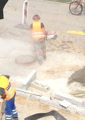 Foto von Arbeitern, die Borde schneiden mit großer Staubentwicklung, ist zu sehen.