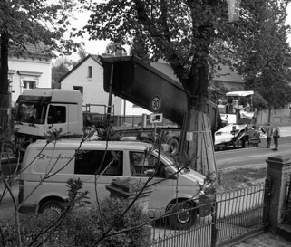 Foto von der im Bau befindlichen Straßenseite mit LKW und Fertiger und Postauto sind zu sehen.