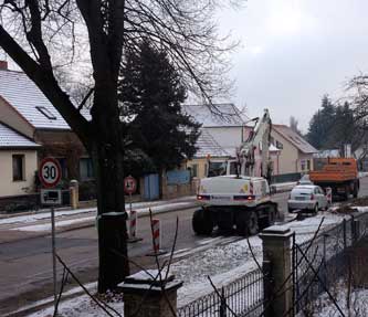 Man sieht einen großen weißen Bagger, der am Straßenrand steht und kurz dahinter dann eine große Linde - aus dem Fenster geschaut